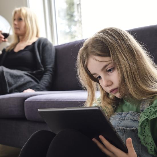 pige med ipad og mor med vinglas i baggrunden