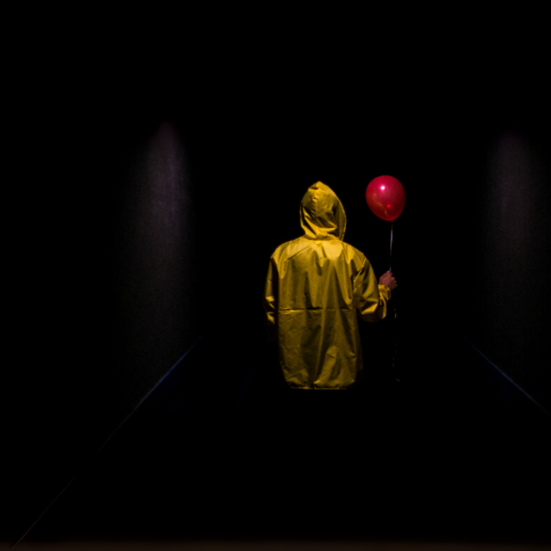 Person med gul regnjakke og rød ballon set bagfra